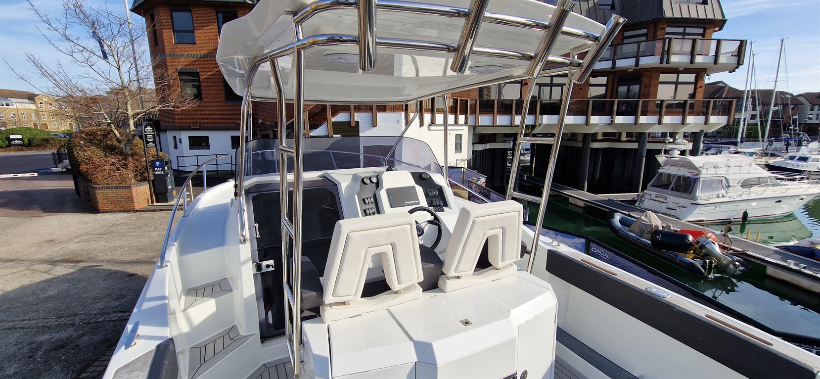 Pilot seat and controls of a white motorboat docked near luxury homes and other vessels in a marina.